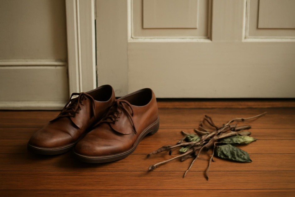 A pair of shoes by a door and a small bundle of twigs and leaves